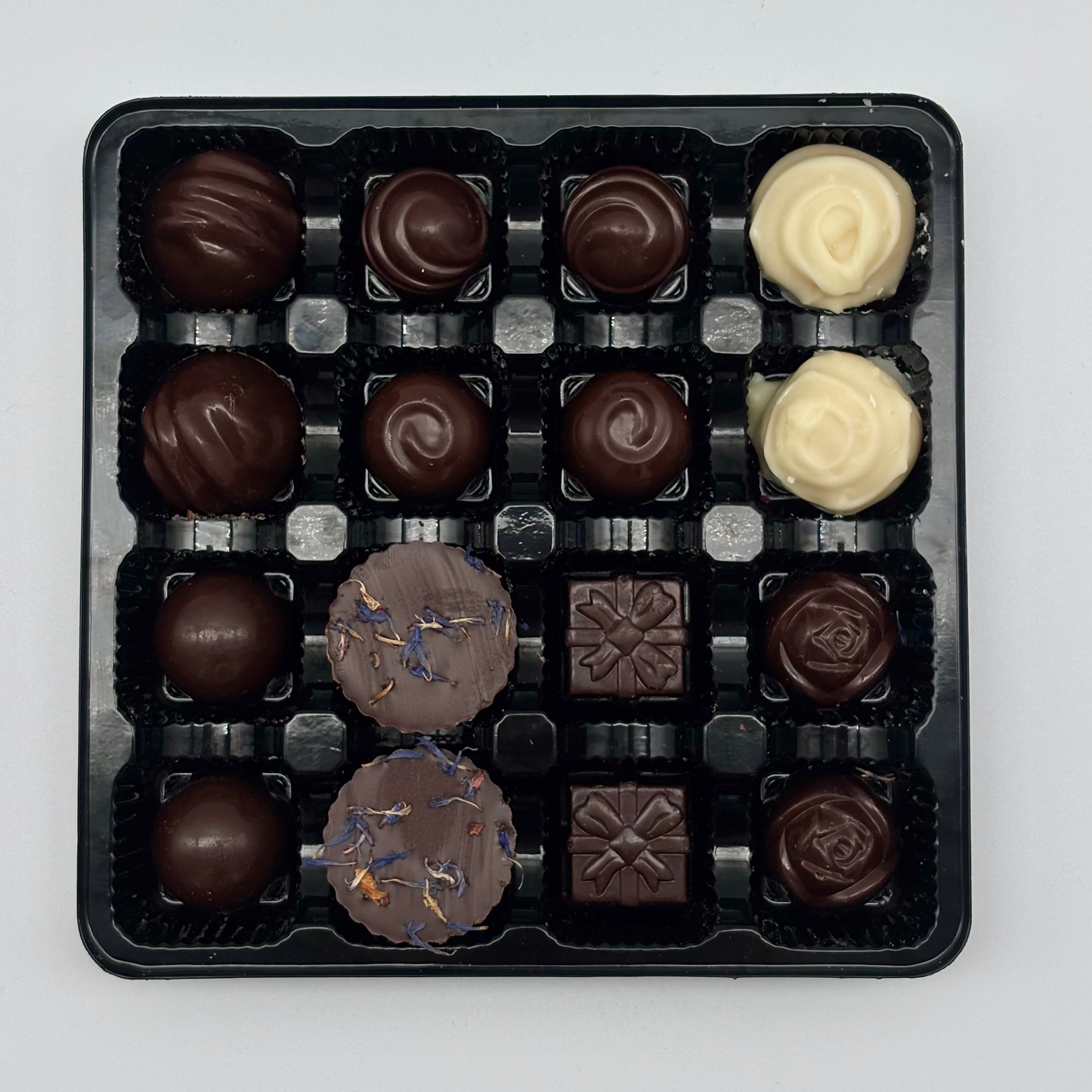 Assorted chocolates in a black plastic tray on a white background