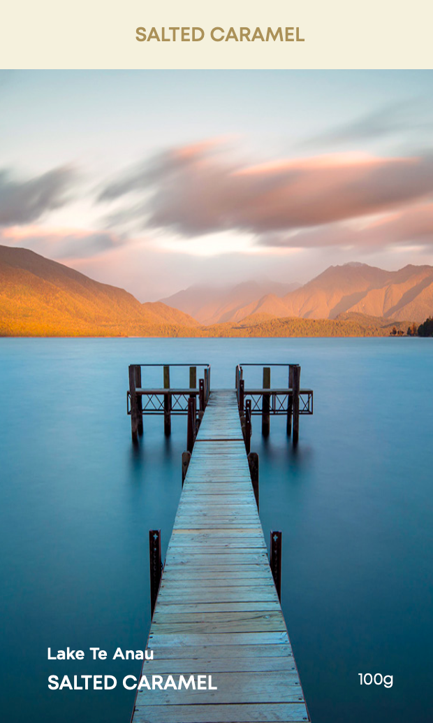 A chocolate block with 'SALTED CARAMEL' text on it, against a backdrop of a lake Te Anau and mountains at sunset.