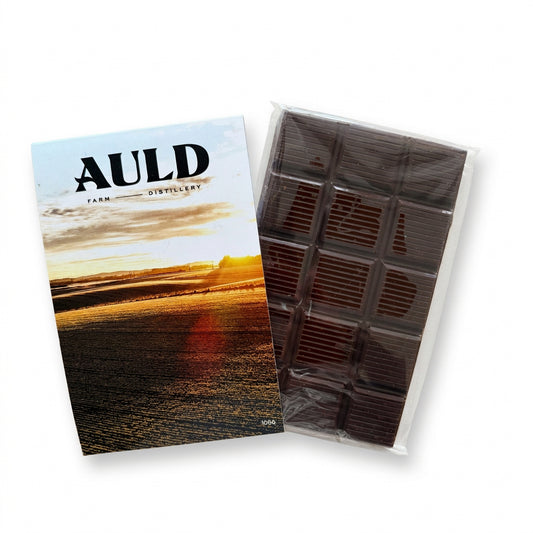 AULD Farm Distillery chocolate bar packaging shown on a light wood surface, with the printed box on the left and the chocolate bar in clear plastic wrapping on the right.