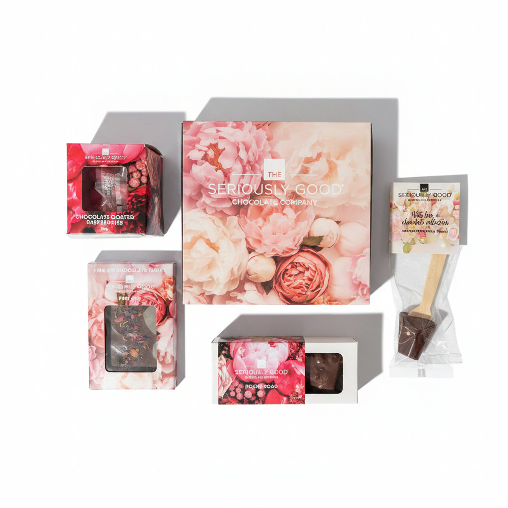 A curated chocolate gift set from Seriously Good Chocolate Company, featuring a large floral box, smaller floral boxes with chocolate windows, a packaged chocolate-coated spatula, and a chocolate bar, arranged on a white background with soft shadows.