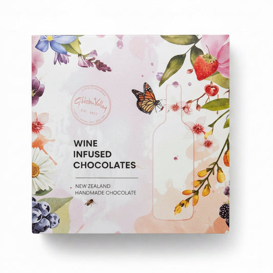 A square box of gibbston valley Wine Infused Chocolates, featuring a light pink background decorated with watercolor illustrations of flowers, a butterfly, and a strawberry. The text 'WINE INFUSED CHOCOLATES' is printed in black on the front.