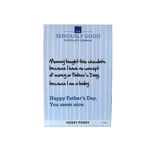A rectangular chocolate bar package from Seriously Good Chocolate Company lies on a light wood surface. The package is white with thin blue vertical stripes and printed text that reads, 'Mummy bought this chocolate because I have no concept of money or Father's Day, because I am a baby.