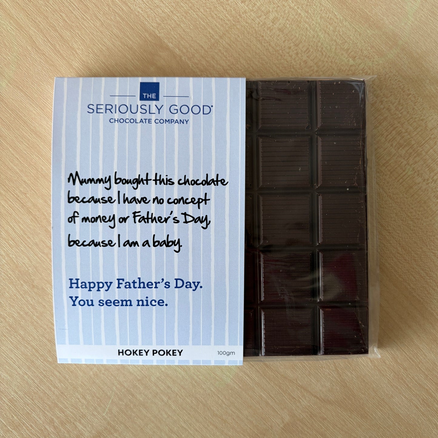 A packaged chocolate bar from Seriously Good Chocolate Company on a light wood surface. The white wrapper has blue text and handwritten-style lettering that says it was bought for Father's Day, with the brand name HOKEY POKEY also visible at the bottom.