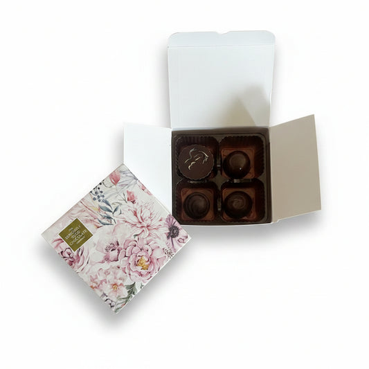 Box of chocolates with a floral card surrounded by pink flowers on a wooden surface