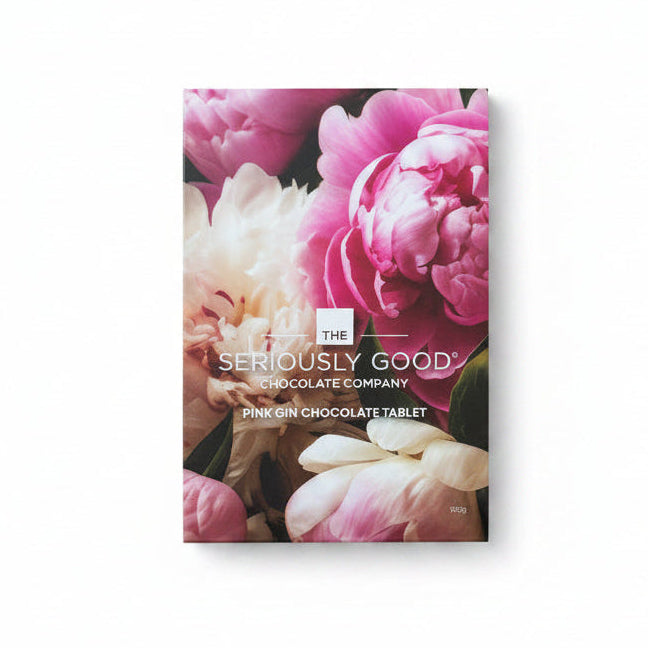 A boxed chocolate product from Seriously Good Chocolate Company lies on a light wood surface. The box features a floral design with large pink and white peony flowers and visible text reading 'SERIOUSLY GOOD CHOCOLATE COMPANY' and 'PINK GIN CHOCOLATE TABLET.