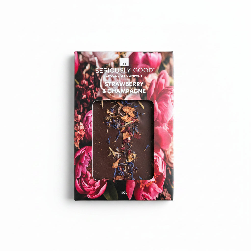 The Seriously Good Chocolate Company Strawberry & Champagne 100g box, featuring a vibrant pink rose floral design and a clear window showing the dark chocolate inside with champagne-colored swirls, set against a light wood background.