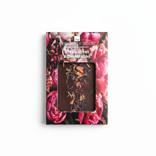 The Seriously Good Chocolate Company Strawberry & Champagne 100g box, featuring a vibrant pink rose floral design and a clear window showing the dark chocolate inside with champagne-colored swirls, set against a light wood background.