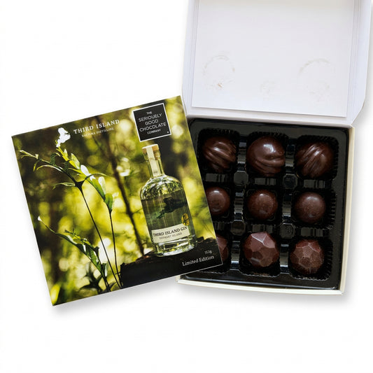 A boxed chocolate gift set from Third Island Distillatory, showing an open white box with dark chocolate truffles in a black tray beside a printed insert card with a bottle photo and green foliage background.