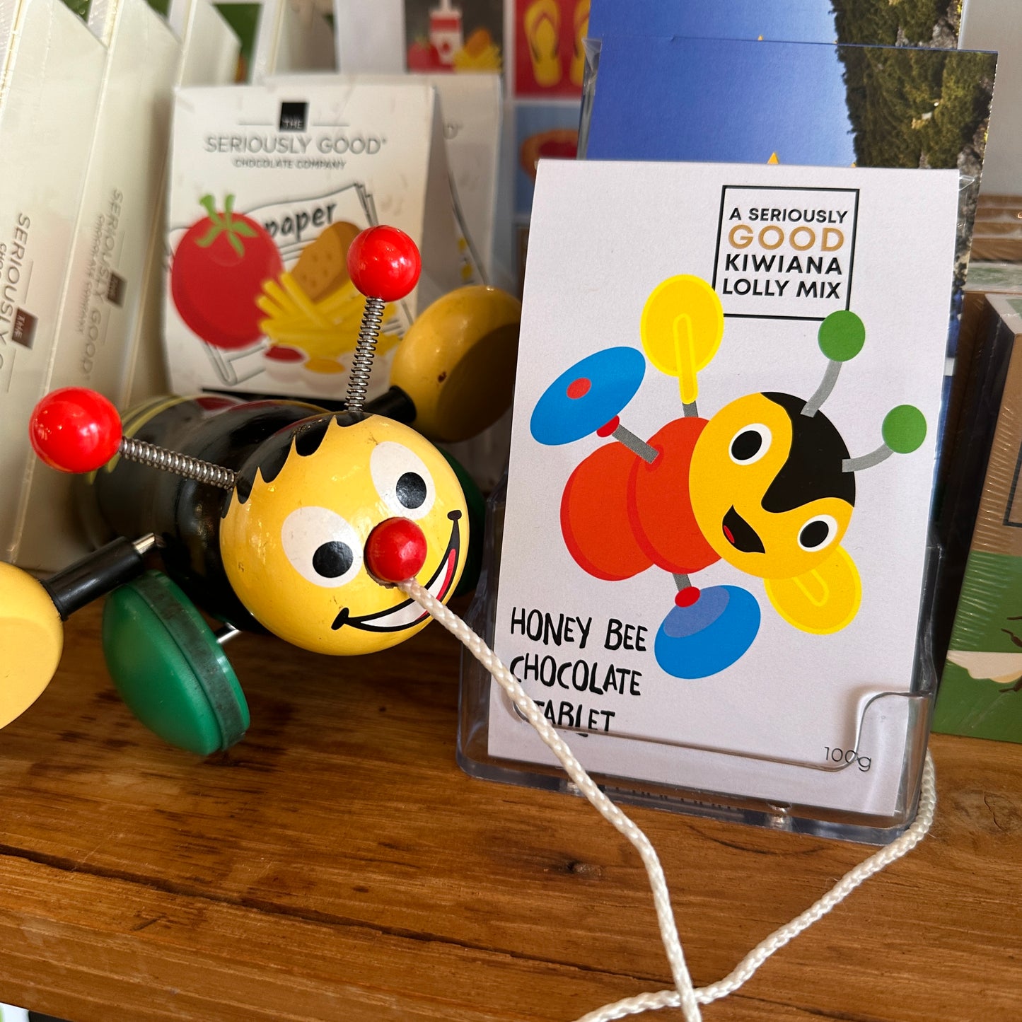A packaged honey chocolate tablet with a bee design, displayed next to a toy honey bee on a wooden surface.