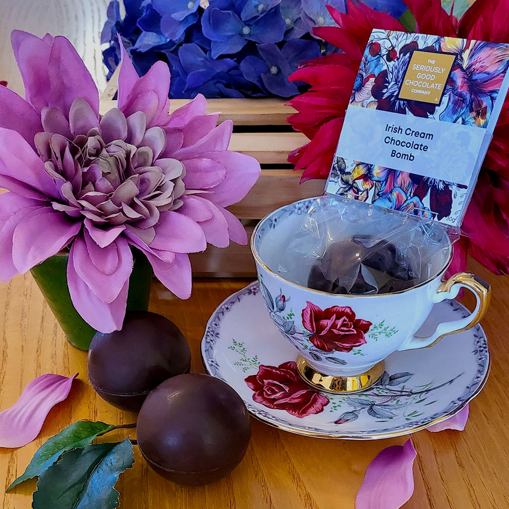 The Seriously Good Chocolate Company Indulgent Hot Chocolate Bomb from the Botanica Collection Handmade in Southland NZ Wrapped chocolate bomb sitting inside floral teacup with 2 unwrapped sitting beside decorated with blue, pink & red flowers & petals