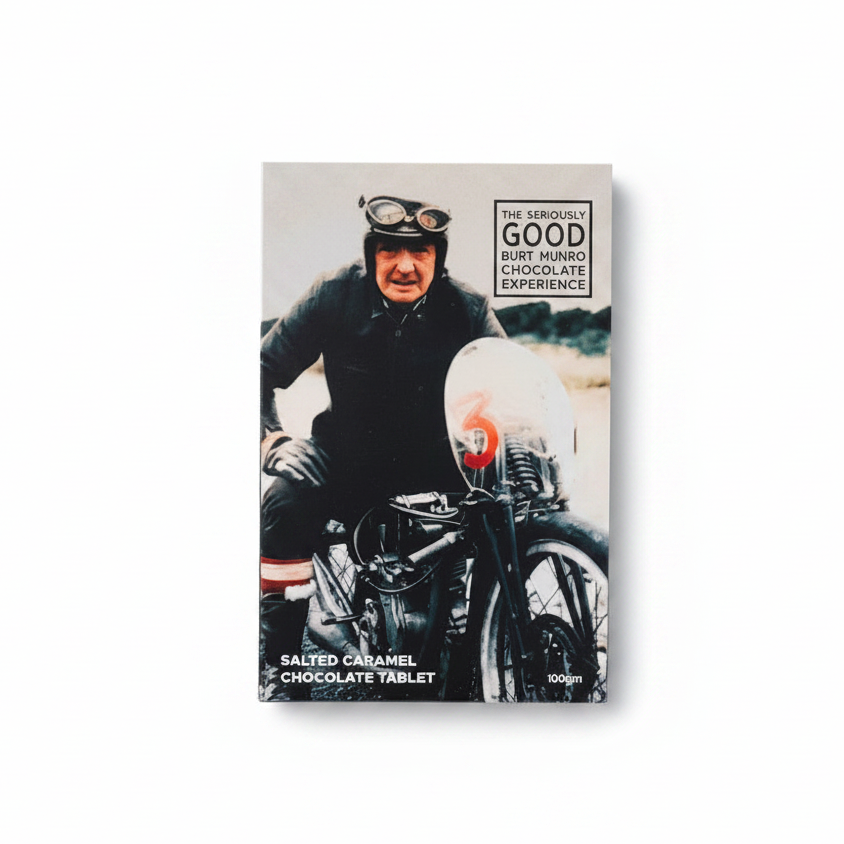 A chocolate block with a printed image of Burt Munro on the packaging, alongside pieces of chocolate and a small metal motorcycle figurine.