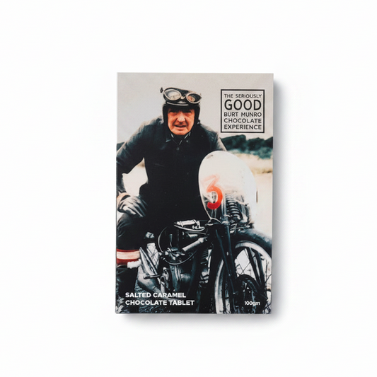 A chocolate block with a printed image of Burt Munro on the packaging, alongside pieces of chocolate and a small metal motorcycle figurine.