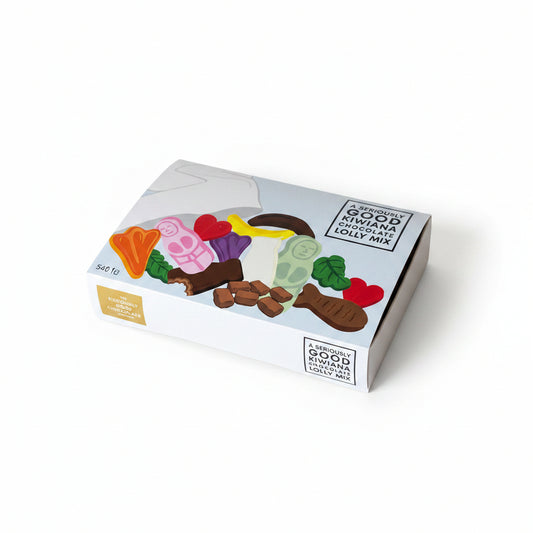 A box of Kiwiana lolly mix with various chocolates around it, placed on a wooden surface.